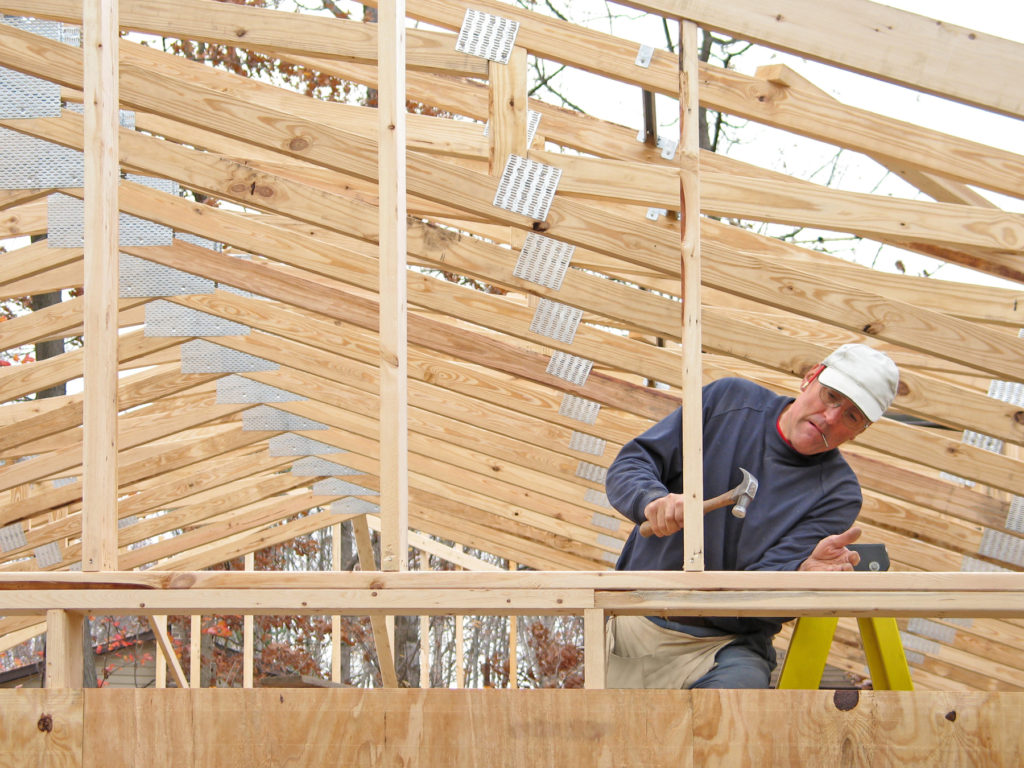 carpenter hammering a wooden roofing frame.