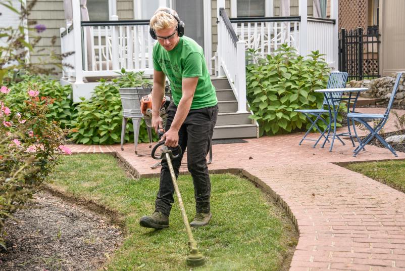 A man trimming a lawn in front of a house using a trimmer.