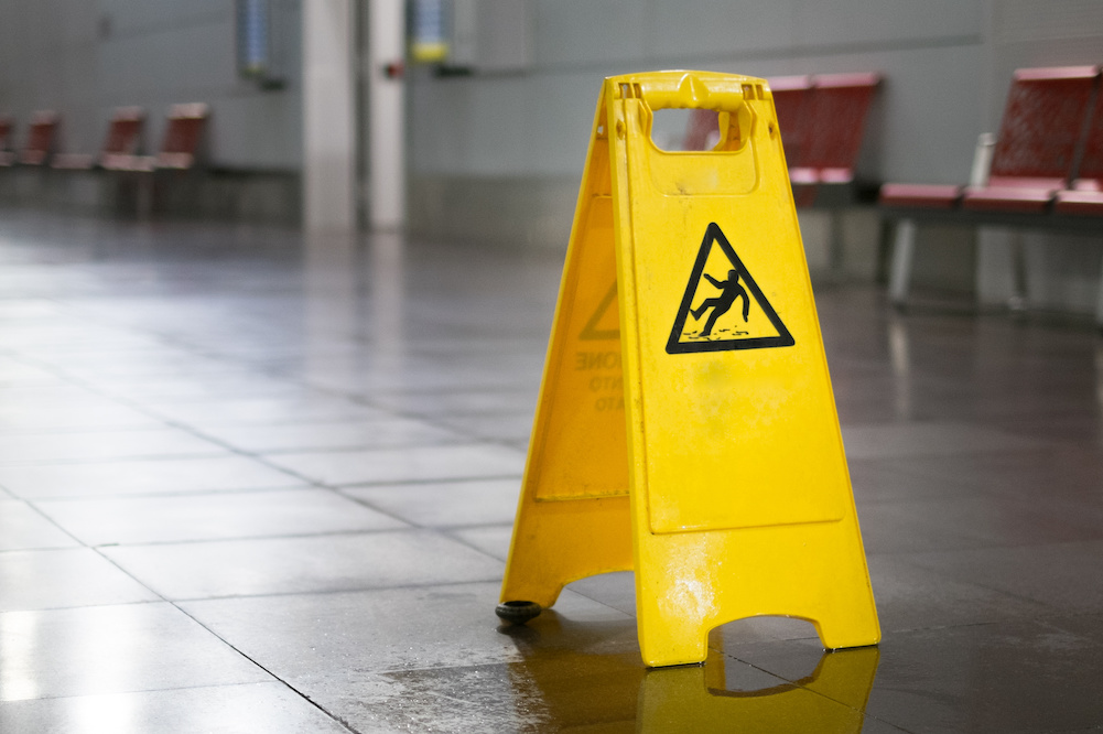 Yellow slip and fall sign on a wet floor with red chairs in the background.