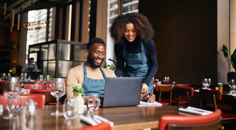 Restaurant managers working with laptop at a table with silverware and glasses.