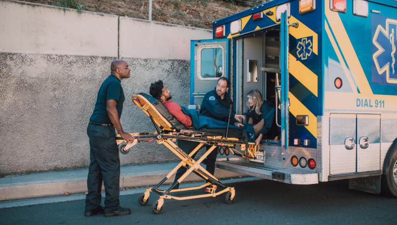 Three EMTs load a patient on a wheeled gurney into an ambulance.