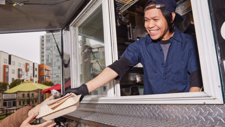 A food truck owner hands a customer their order.