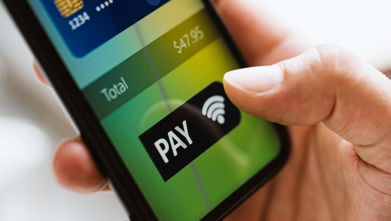 Close-up shot of a hand holding a mobile phone. The phone displays a payment app interface.