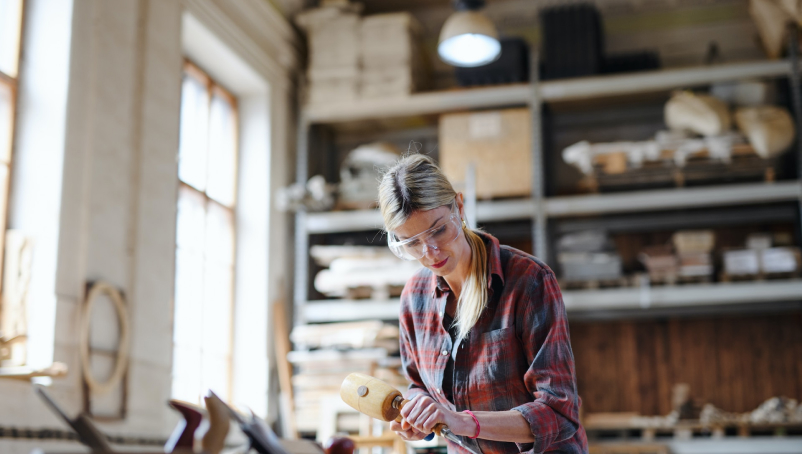 A woodworker, using a mallet and chisel, works in a workspace.