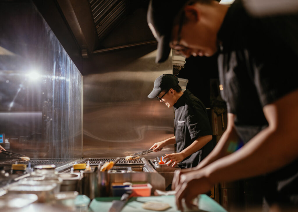 two uniformed restaurant workers cooking food