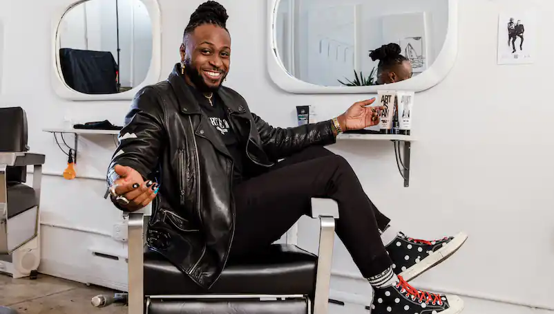 A smiling person sits in a salon chair in front of a mirror in a hair salon