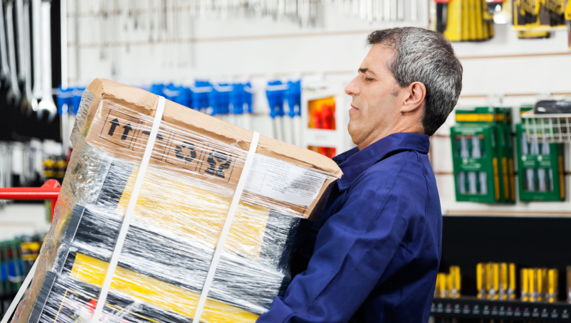 A worker carrying a heavy tool package in a hardware store.