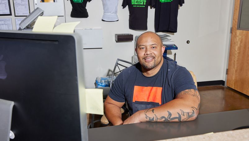 person sits in front of a computer covered in sticky notes in front of a wall of t-shirts