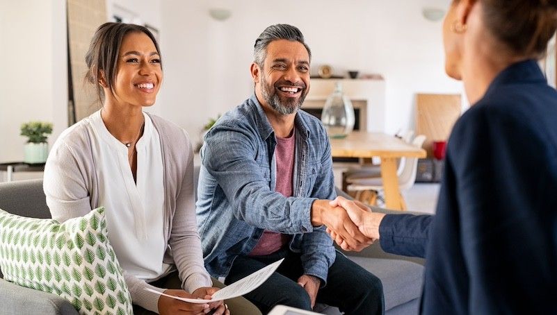 Two small business owners smile and shake hands with a business insurance claims adjuster