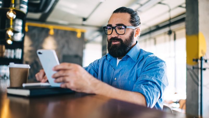 Smiling small business owner sits near bar using a smartphone.