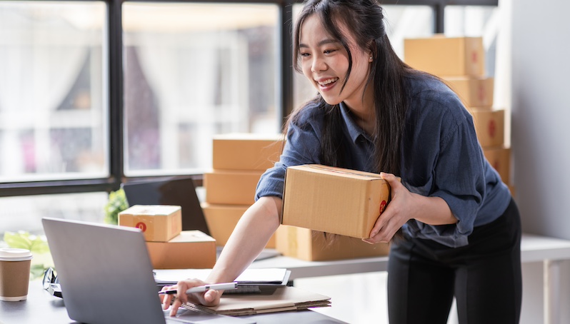 Person holding a shipping box using a laptop computer in an office